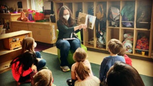 preschool educator reading a picture book to group of students on carpet